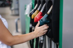 Mulher com a mão direita em uma das bombas de gasolina, representando o aumento do ICMS e reajuste dos preços dos combustíveis